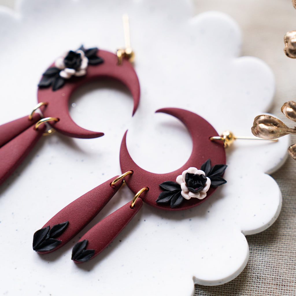 Red crescent moon-shaped earrings with floral details on a decorative white plate.