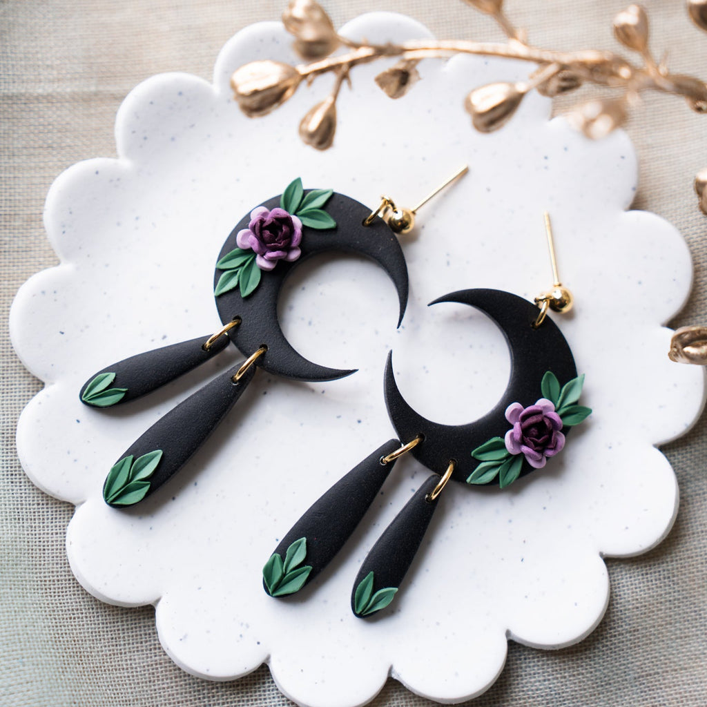 Black crescent moon earrings with floral details on a white dish.
