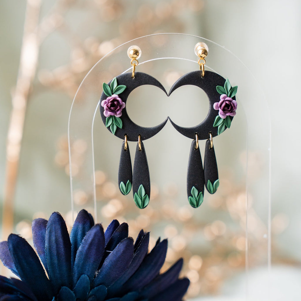 Black earrings with floral designs on a clear stand against a blurred natural background